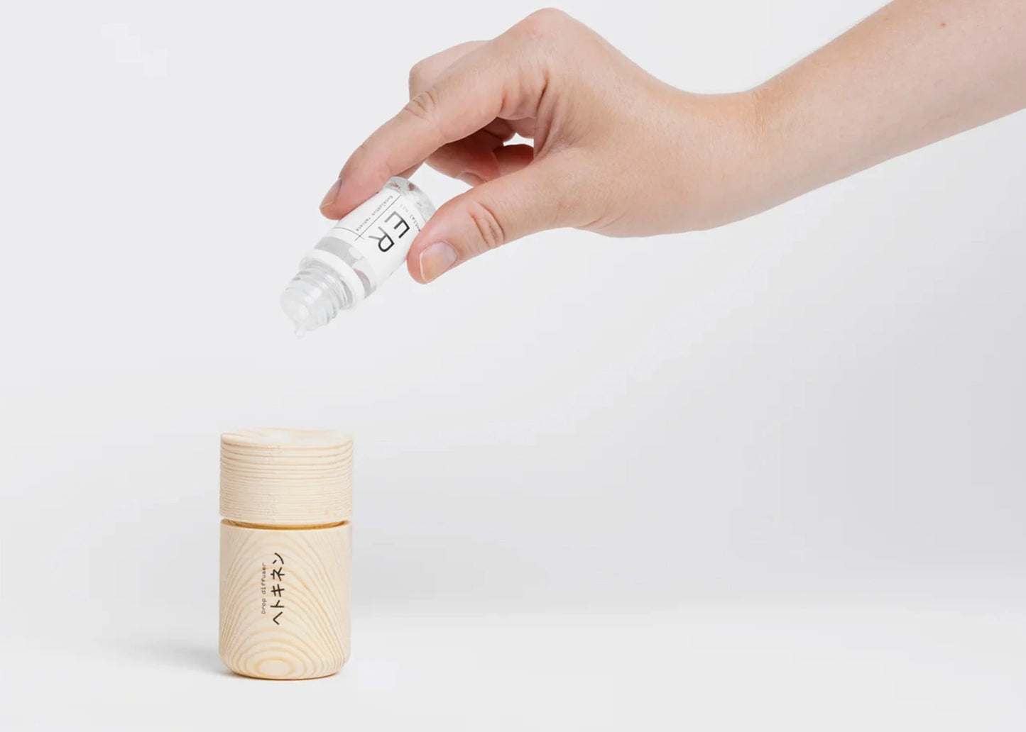 A hand dropping a scent drop onto the Tall Scent Drop Diffuser by Hetkinen