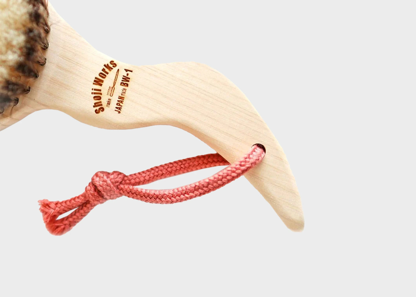 A close up of the Shoji Works hand held short body brush in a light wood color with a pink rope string as sold by Woodland Mod