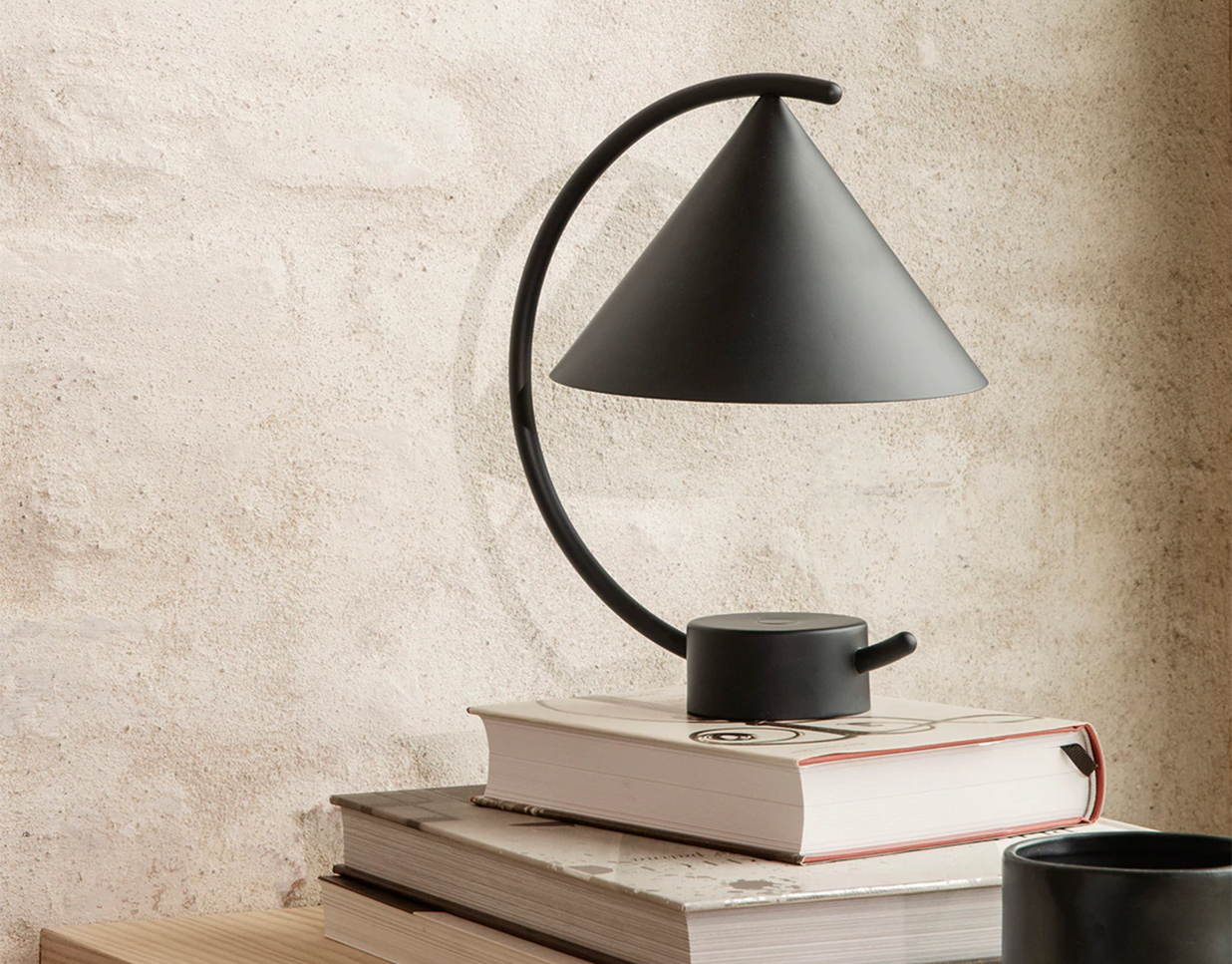 The Black Meridian Lamp by Ferm living resting on a book against a concrete wall