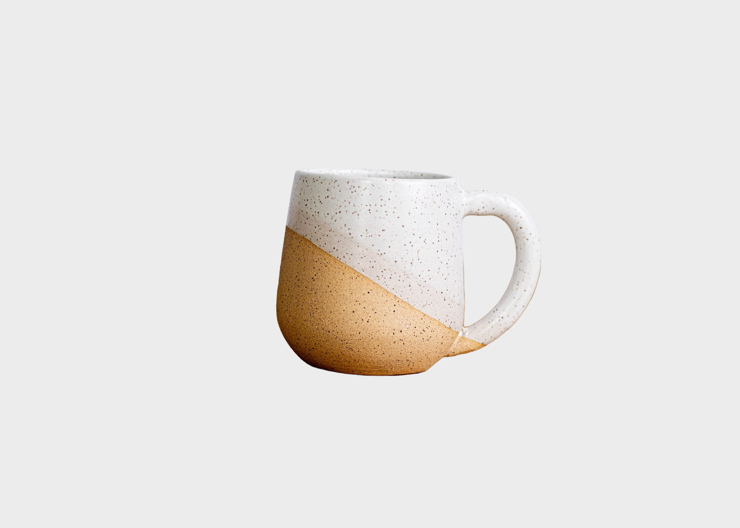 
                  
                    A ceramic mug with a diagonal split design, featuring a speckled white upper half and a warm tan-brown lower half, set against a solid light gray background.
                  
                