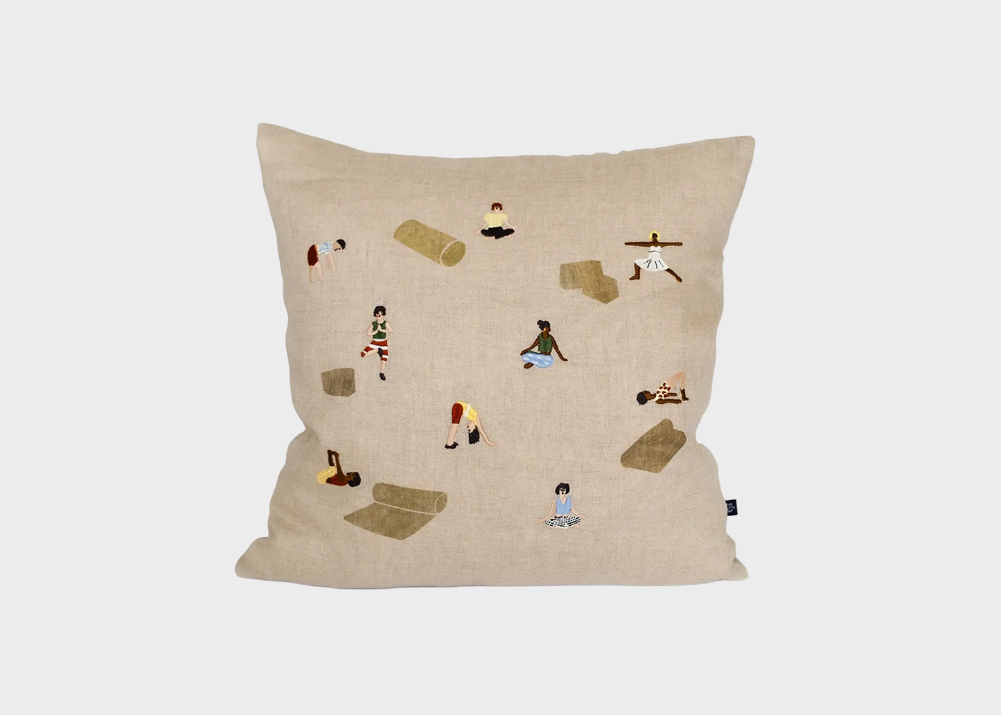 A square beige throw pillow featuring a whimsical embroidered pattern of small figures, mats, and exercise equipment, shown against a neutral light gray background.