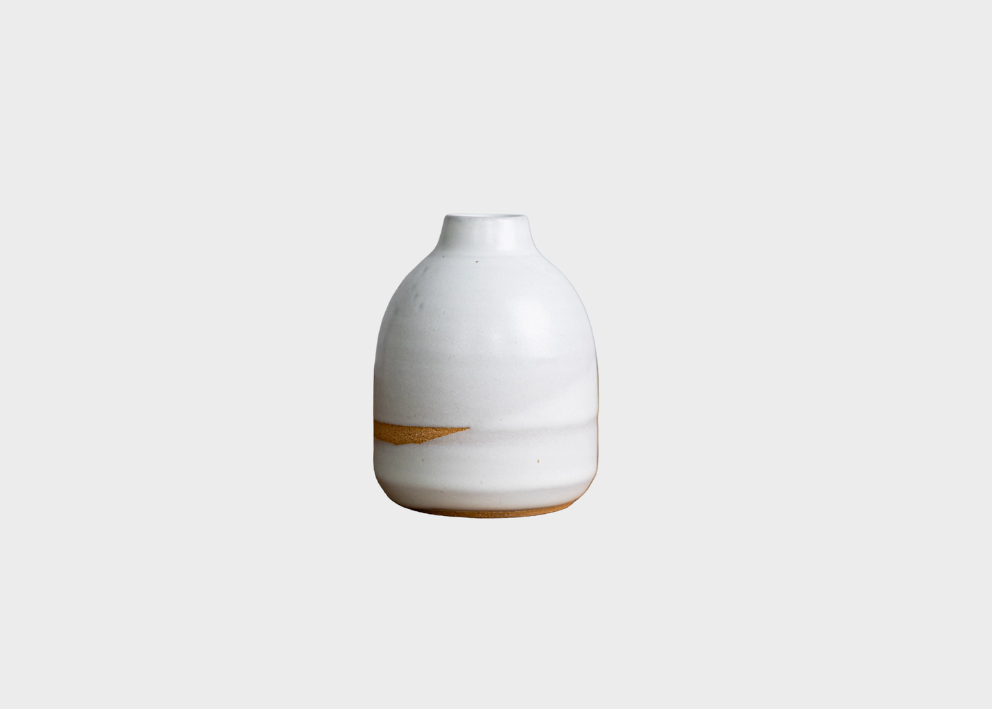 
                  
                    A small ceramic vase with a rounded bulbous body, a narrow neck, and a glossy white glaze, featuring a subtle diagonal brown band near the base, set against a solid light gray background.
                  
                