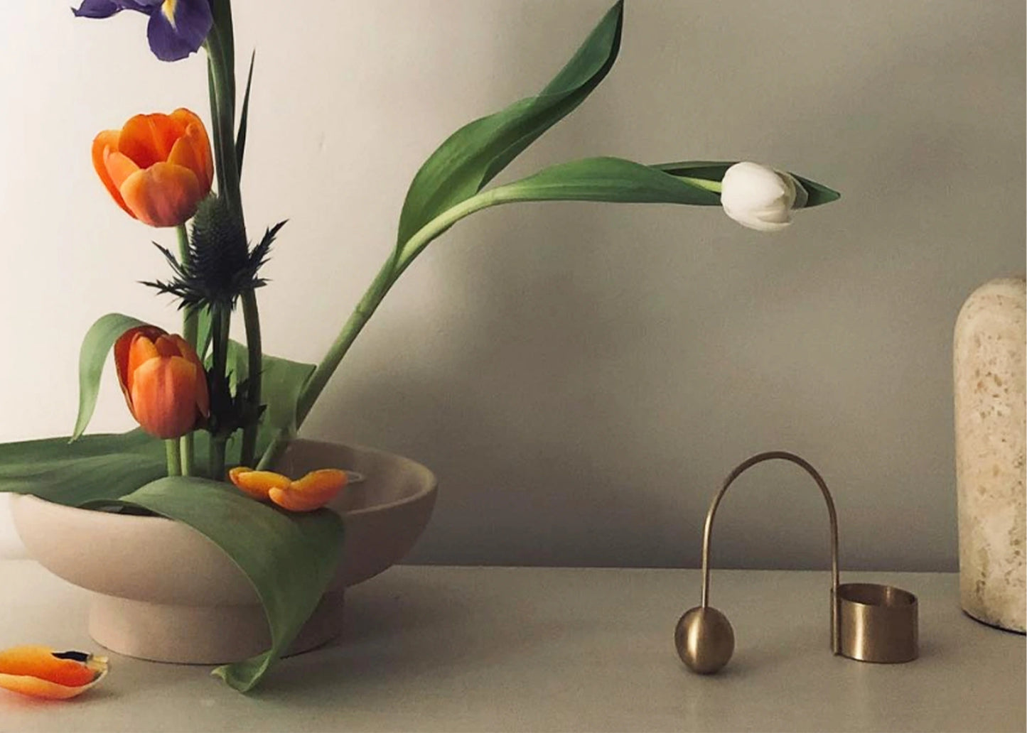 A brass balance tealight holder on a table next to a bouquet of flowers in a bowl.