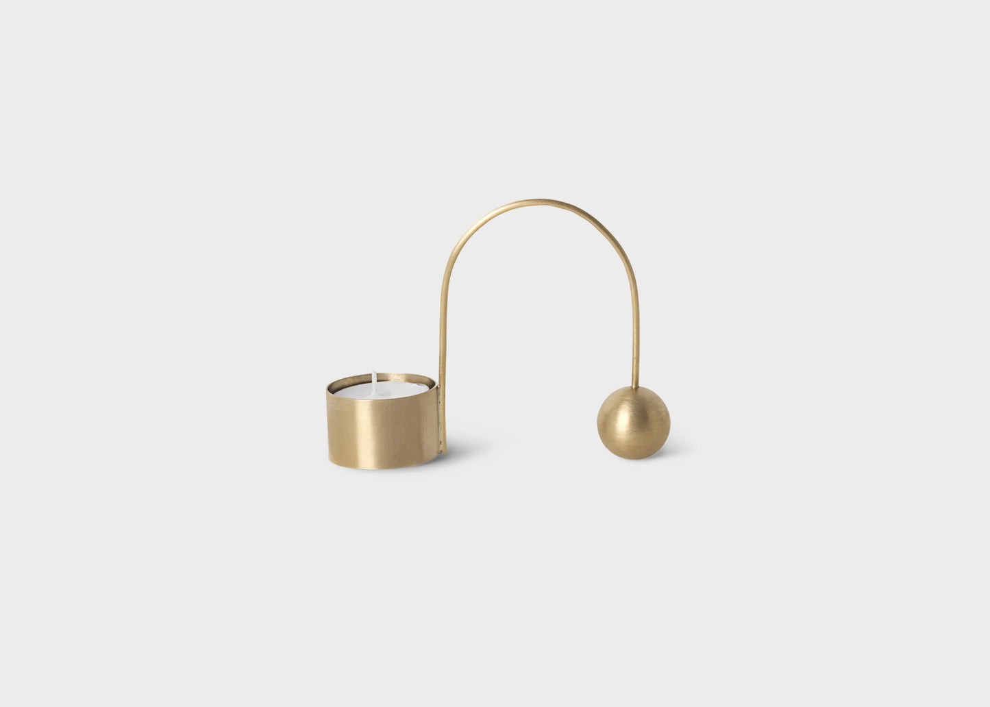 A golden brass balance tealight candle holder by Ferm Living with a tealight candle in it.