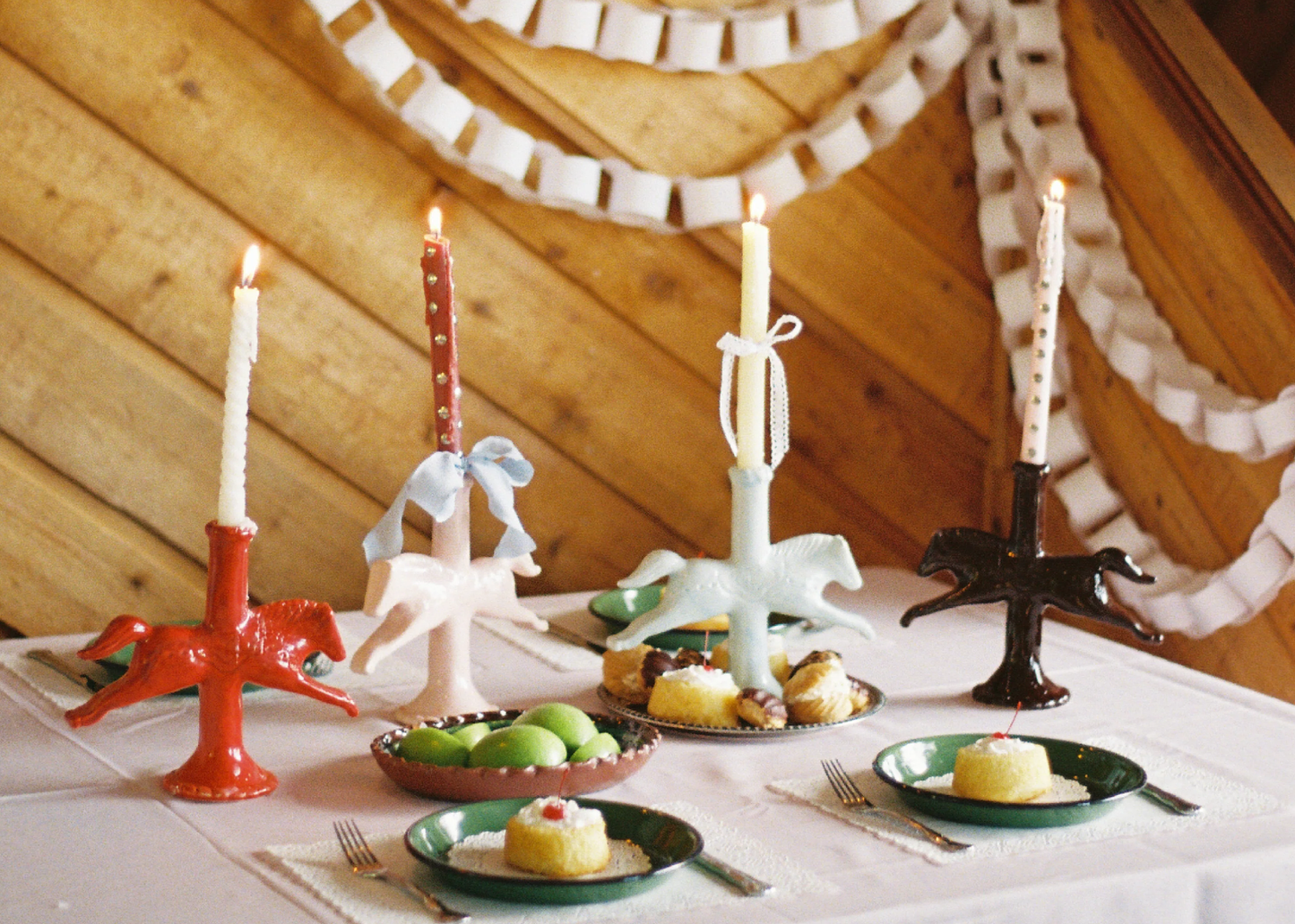 A table full of cakes and fruits, with dala horse candle holders, some with ribbons tied in bows around them
