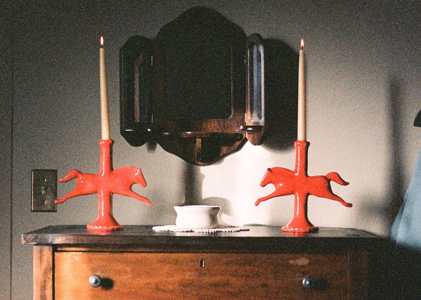 
                  
                    A wooden dresser with a wooden mirror behind it, with two dala horse candle holders with lit candles inside of them. 
                  
                