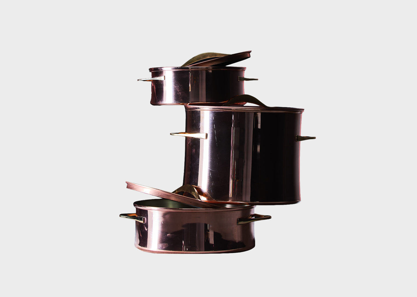 
                  
                    A set of four nested copper pots with matching lids, arranged in a stacked, staggered layout against a solid light gray background.
                  
                