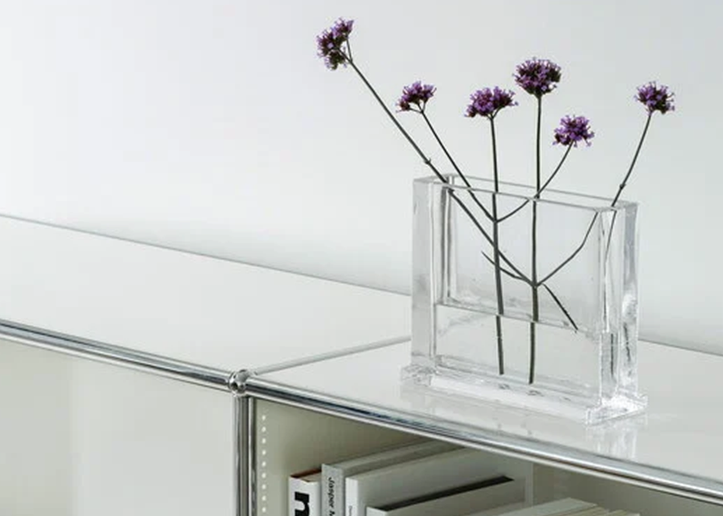 
                  
                    Clear glass vase with purple flowers on a reflective surface
                  
                
