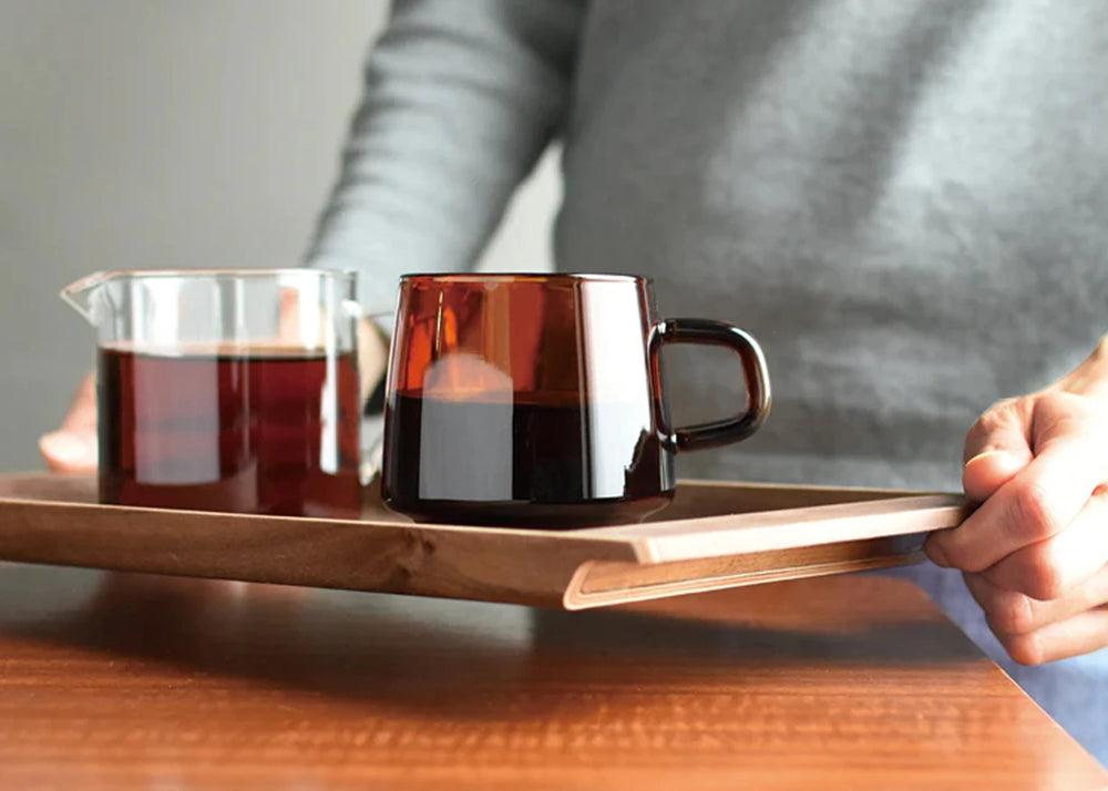 Someone holding the Sepia non slip tray by KINTO with Sepia mugs filled with liquid resting on the tray.