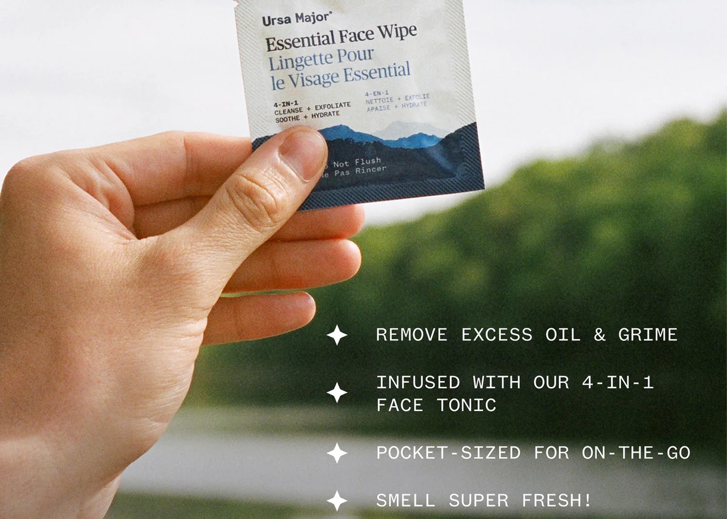 
                  
                    A hand holds a single Ursa Major Essential Face Wipe packet in front of a blurred outdoor background with greenery and a light sky. White text on the right lists product benefits: remove excess oil and grime, infused with 4-in-1 face tonic, pocket-sized for on-the-go use, and super fresh scent.
                  
                