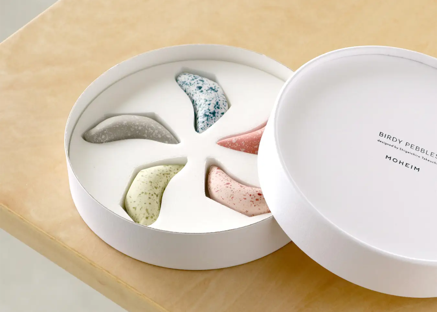 White container with colorful pebbles on a light wooden surface