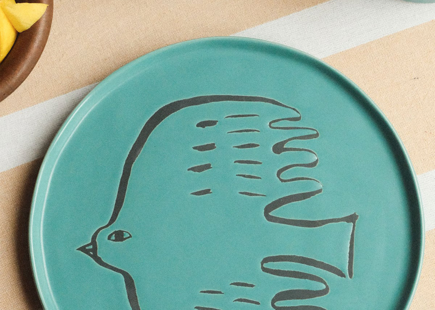 
                  
                    Teal ceramic plate with a bird design on a striped fabric background
                  
                