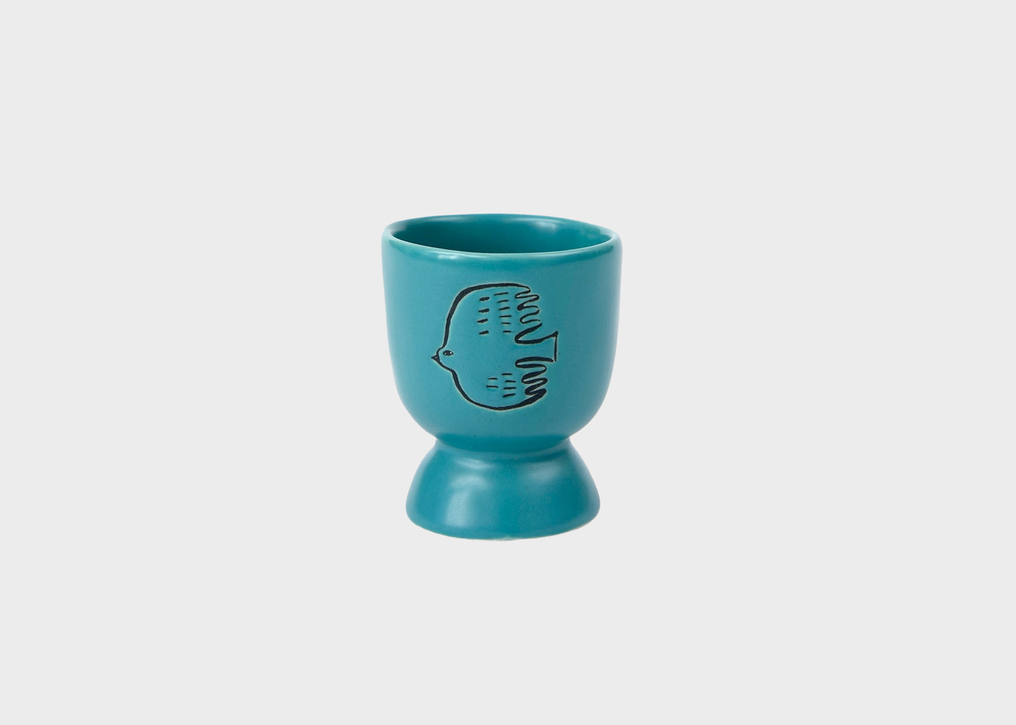 
                  
                    A turquoise blue ceramic egg cup with a matching base and a black line-art bird design on the front, set against a solid light gray background.
                  
                
