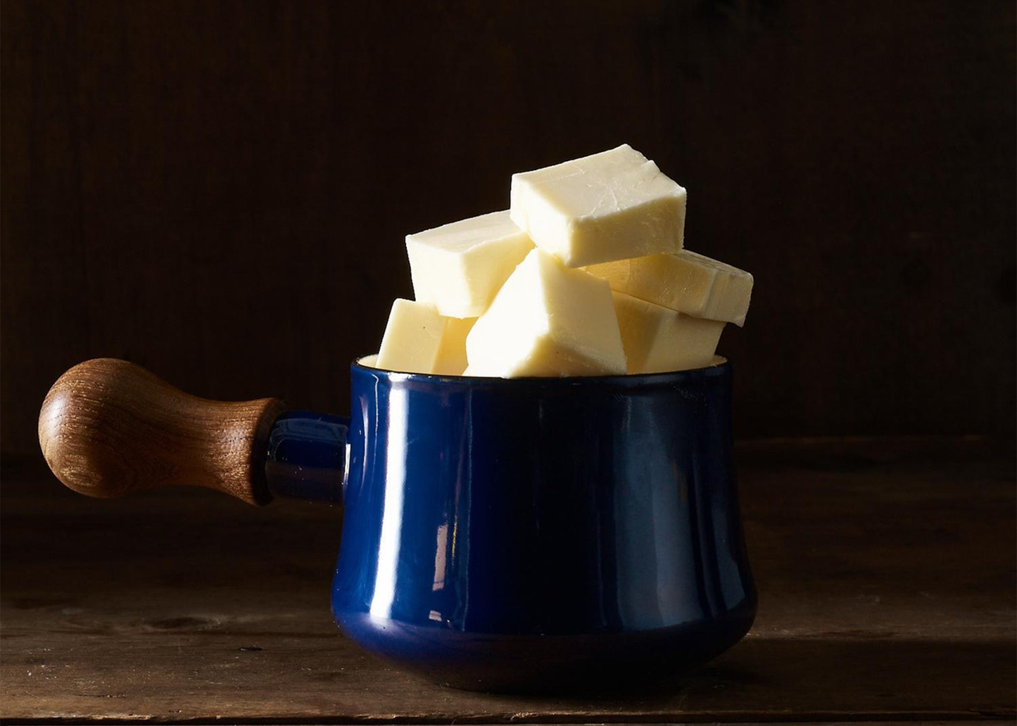 
                  
                    Blue enamel Dansk pot with wooden handle filled with butter cubes on a dark background
                  
                
