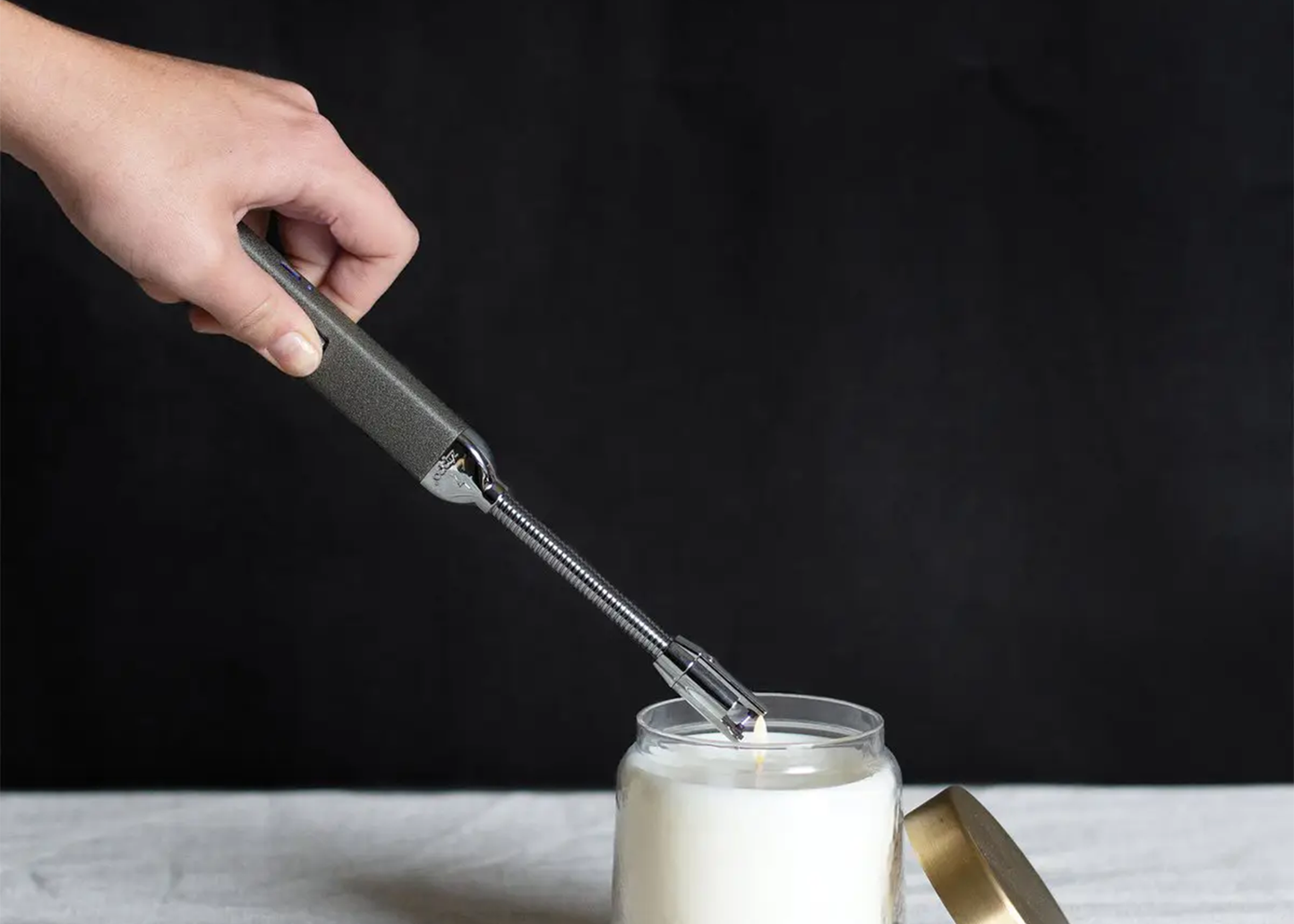 
                  
                    Hand using a candle lighter to light a candle against a dark background
                  
                