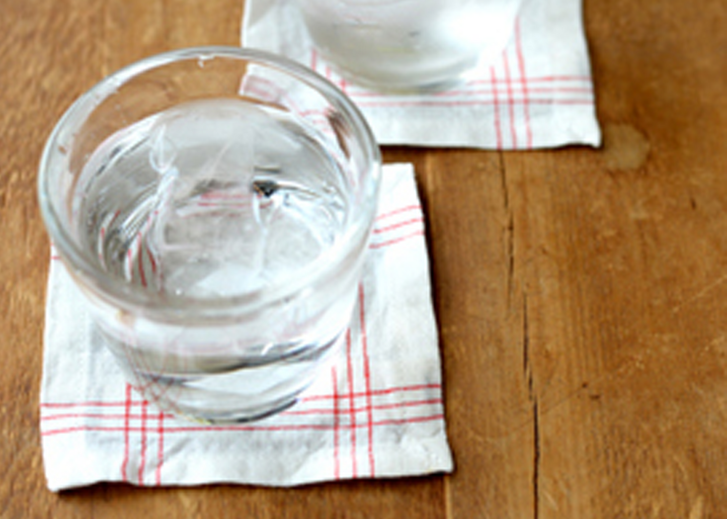 Two glasses of water on checkered coasters on a wooden surface