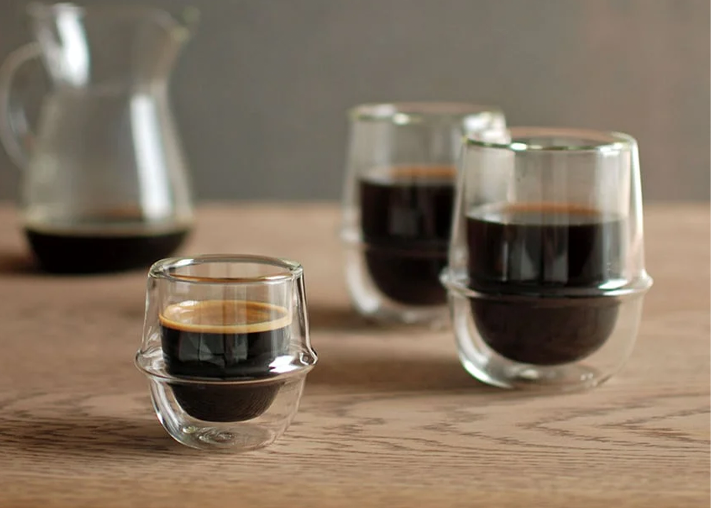 Three glass cups filled with espresso on a wooden surface.