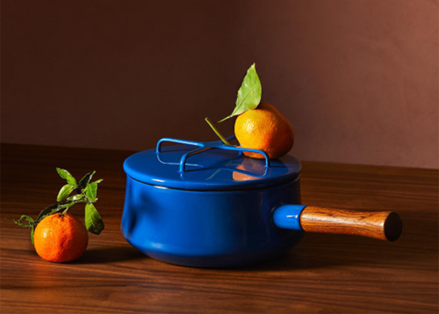 
                  
                    Blue Dansk enamel pot with wooden handle on a wooden surface with oranges and leaves.
                  
                