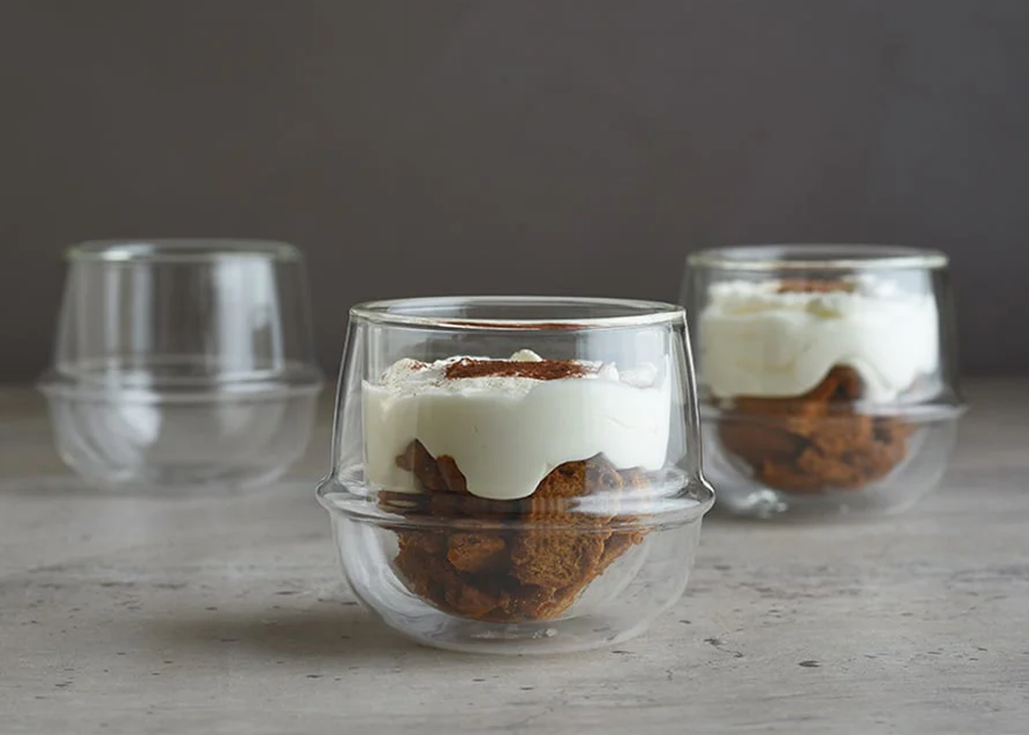 
                  
                    Three glass dessert cups with layered desserts on a wooden surface.
                  
                