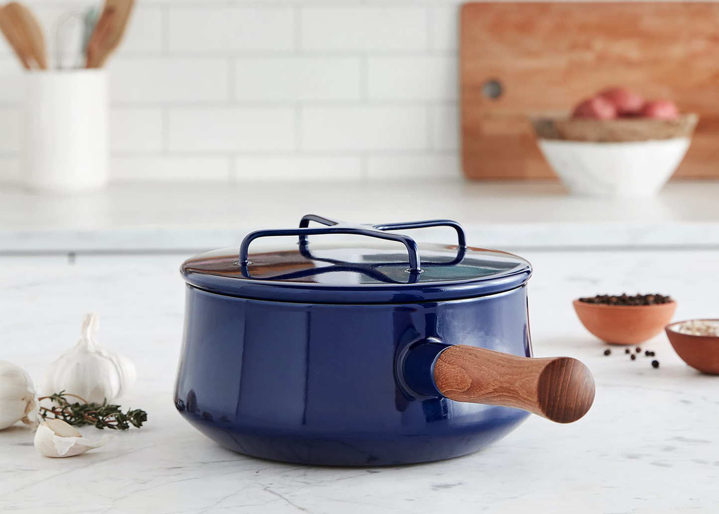 
                  
                    Blue Dansk enameled cast iron cookware with wooden handle on a kitchen counter.
                  
                