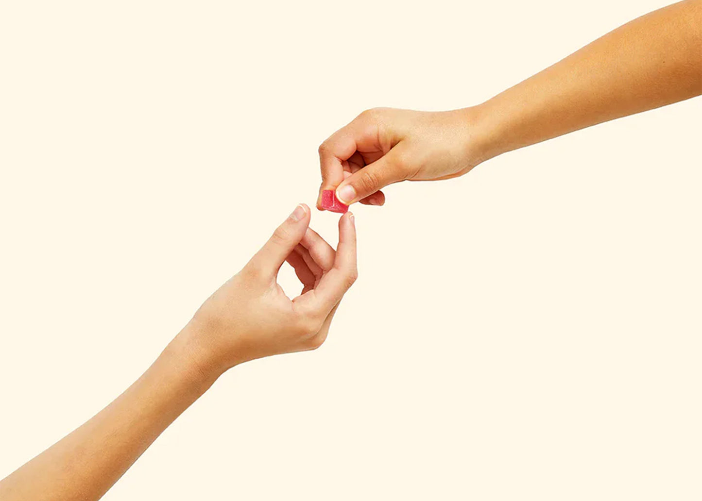 
                  
                    Two hands exchanging a pink mochi issei candy on a beige background
                  
                