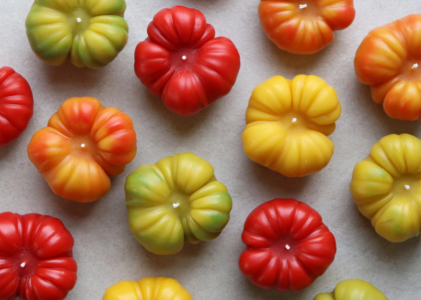 Colorful heirloom tomato-shaped candles on a neutral background