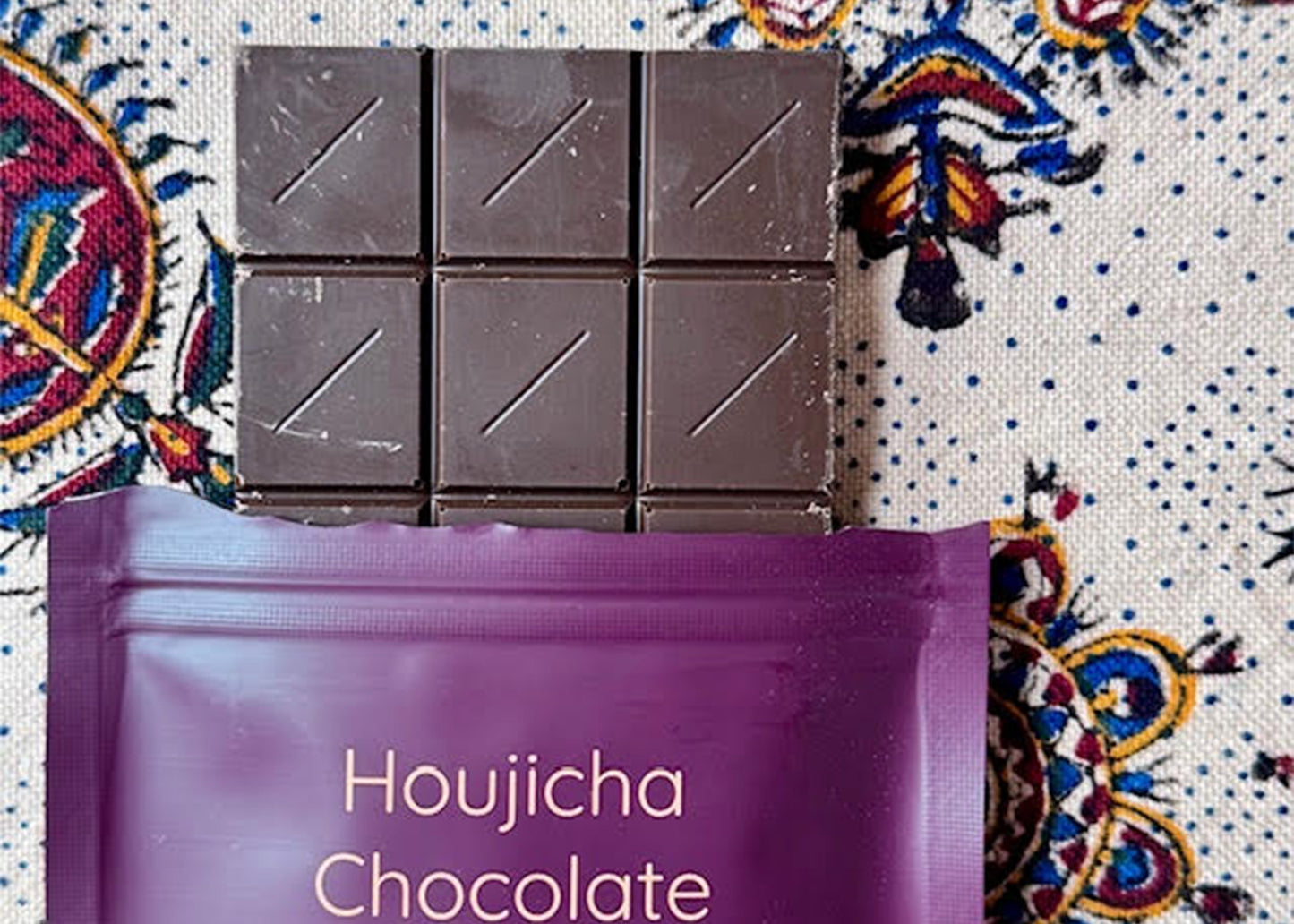 
                  
                    Dark chocolate bars  by kettl on a purple 'Houjicha Chocolate' packaging against a colorful patterned background
                  
                