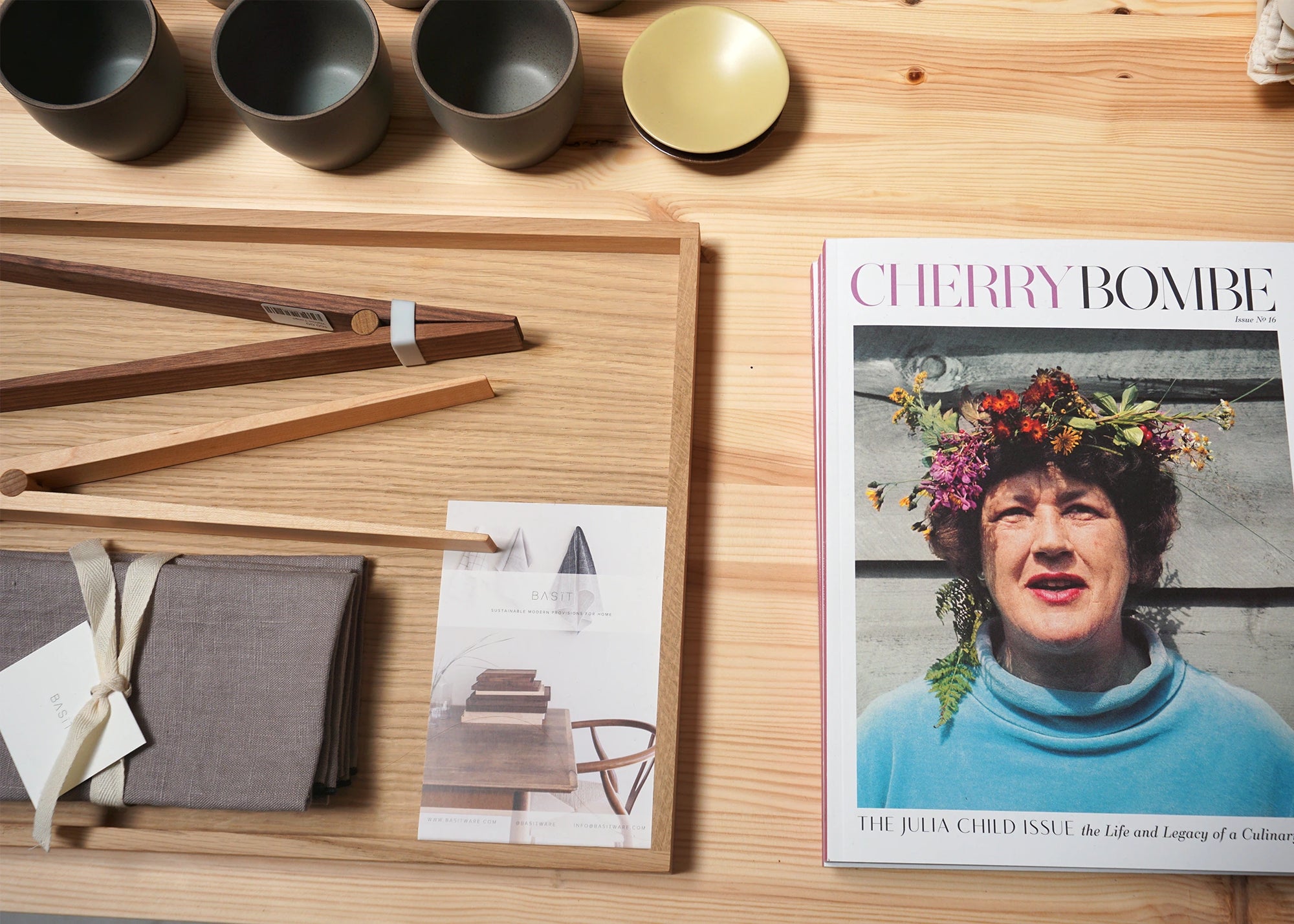 Minimalist wooden chopping board, salad tongs, and a magazine on display in Woodland Mod