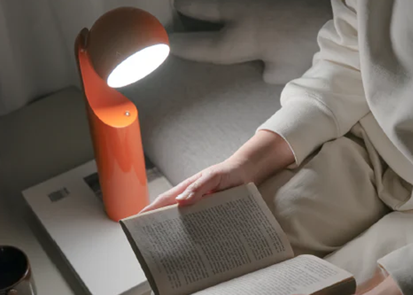 
                  
                    Person reading a book illuminated by an orange lamp on a table.
                  
                