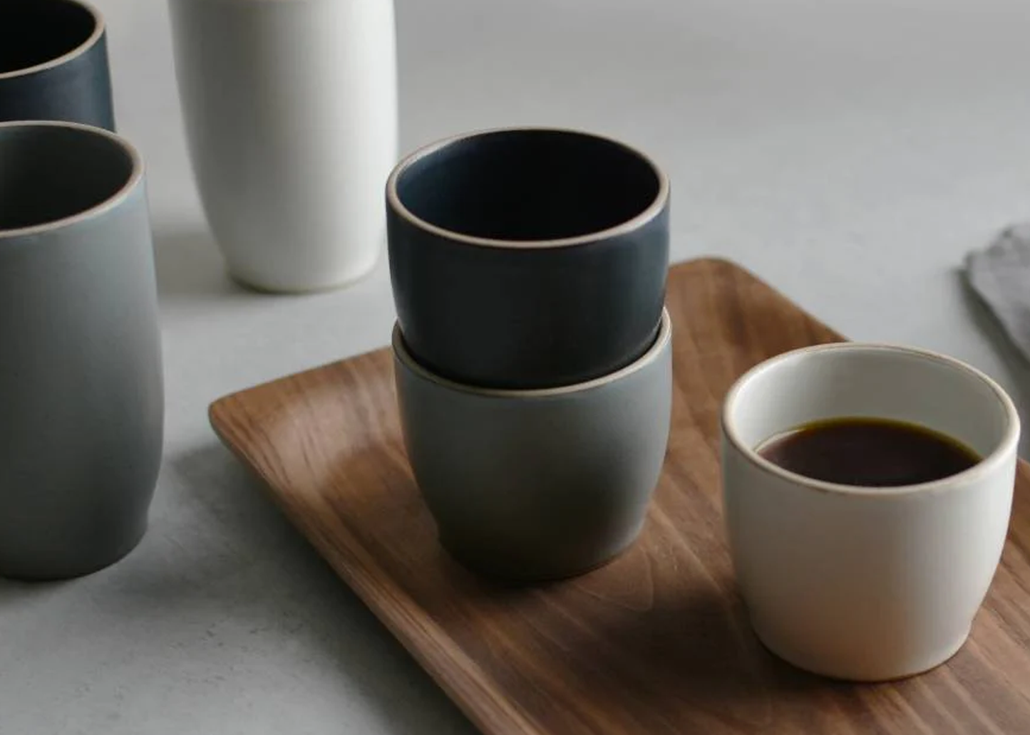
                  
                    Set of ceramic cups on a wooden tray with one cup containing coffee.
                  
                
