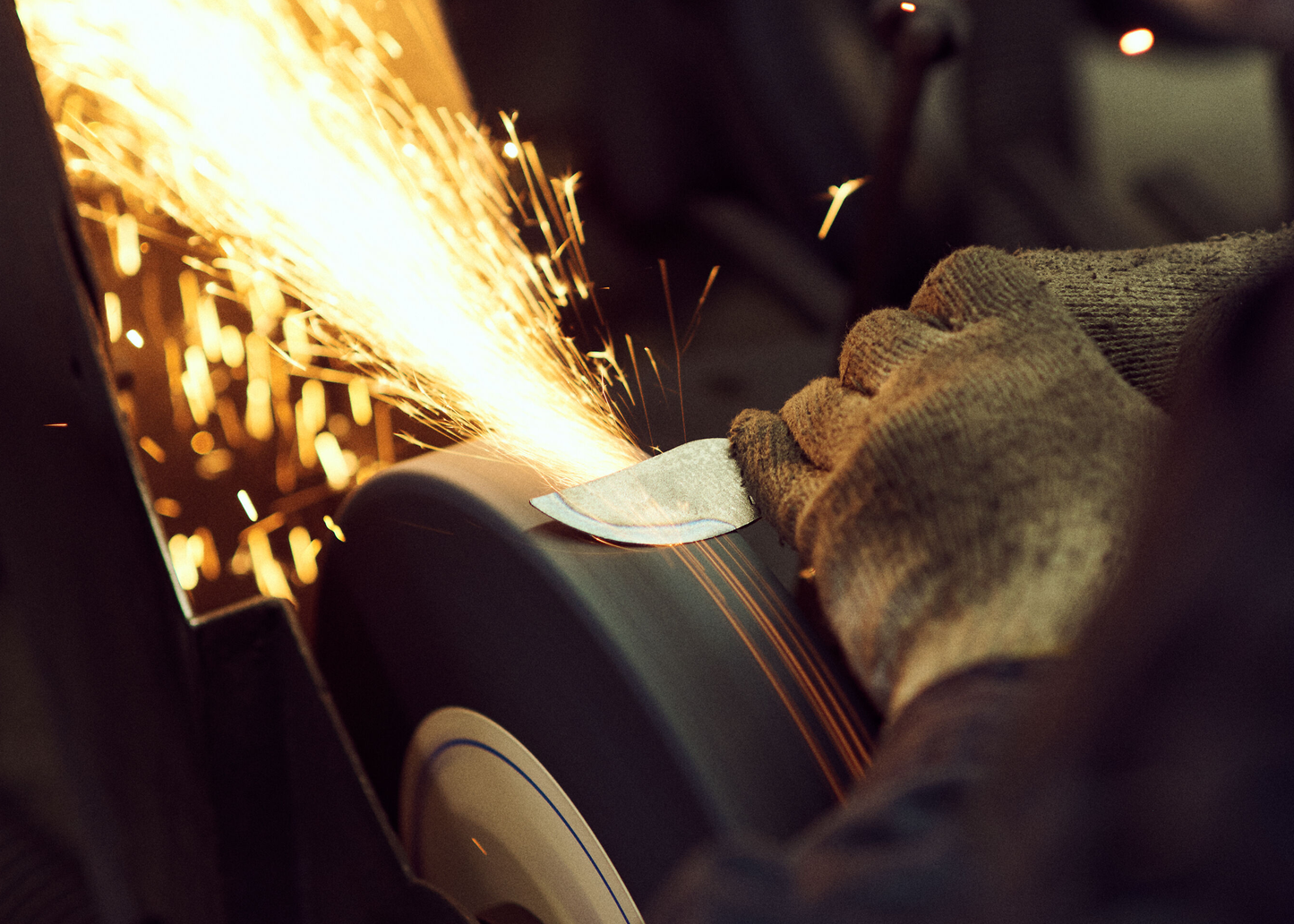 
                  
                    Person wearing gloves using a tool with sparks flying, likely in a workshop setting.
                  
                