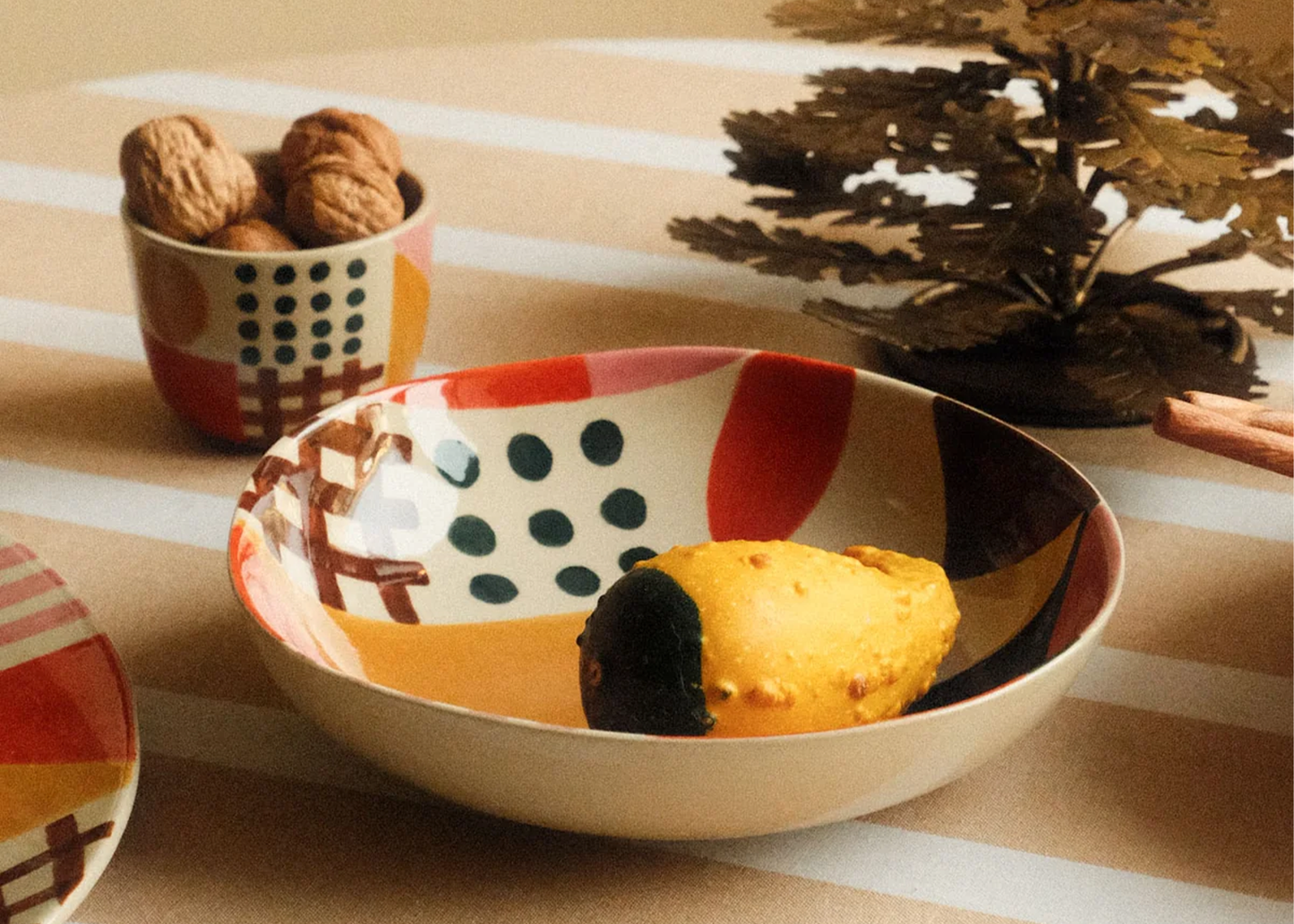 Decorative bowl with polka dot pattern containing a gourd, placed on a striped surface with a tree in the background.