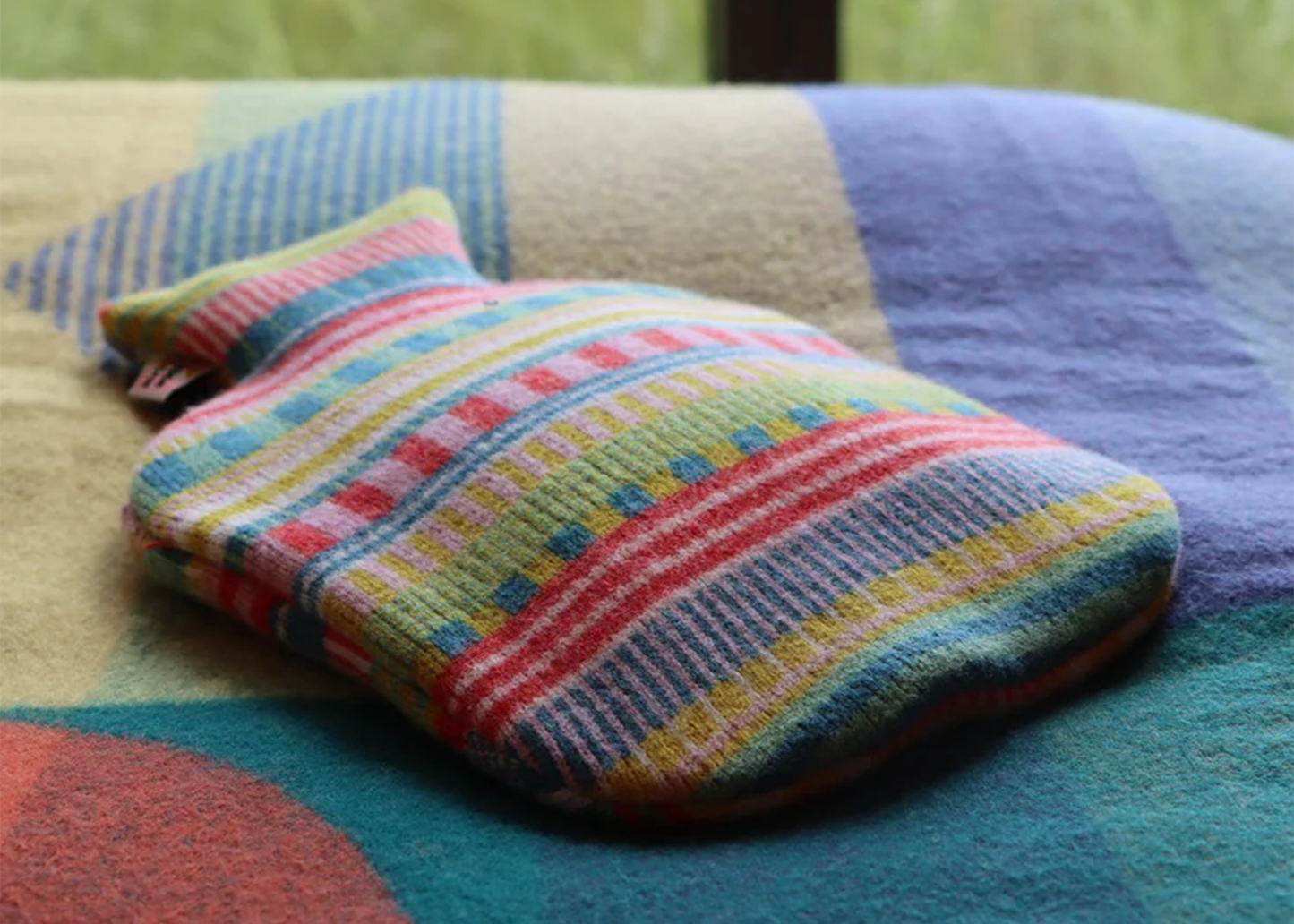 Colorful striped hot water bottle cover on a patterned fabric surface