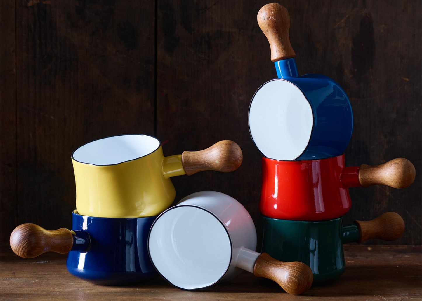 
                  
                    Colorful enamel pots with wooden handles on a wooden surface against a dark background
                  
                