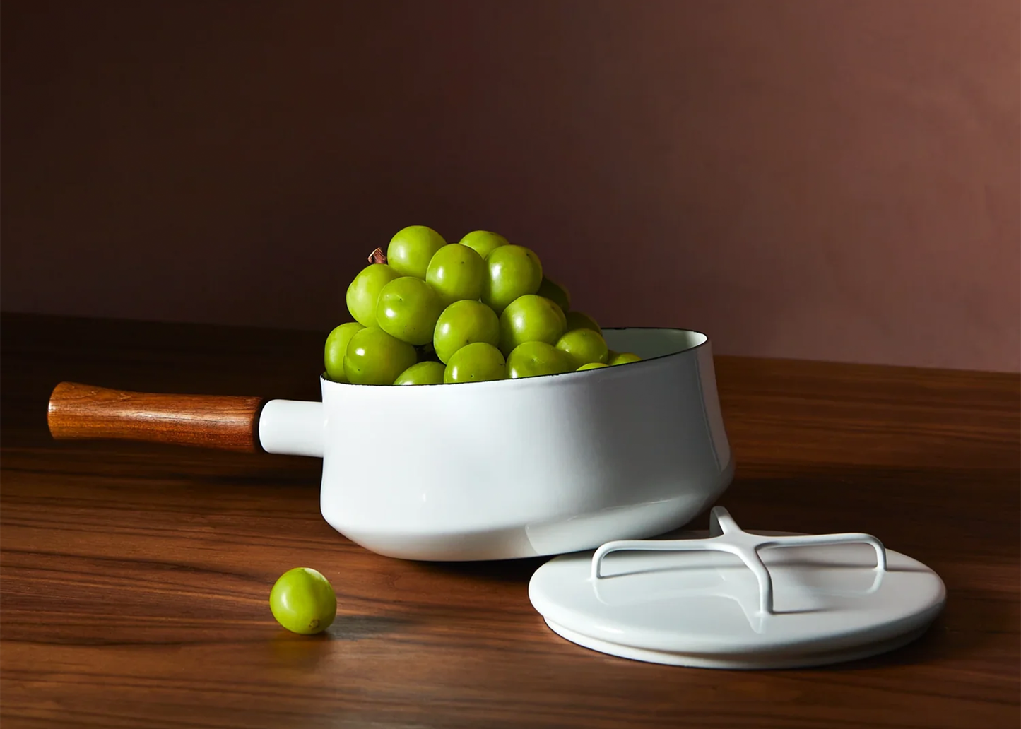
                  
                    White enamel Dansk pot with wooden handle filled with green grapes on a wooden surface.
                  
                