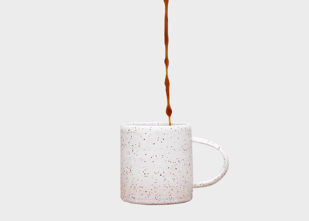 Coffee being poured into a white speckled ceramic mug with a thin handle.