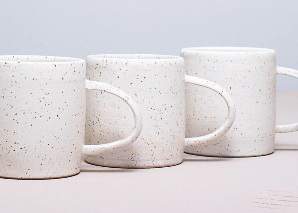 A row of white speckled ceramic mugs with handles facing to the left