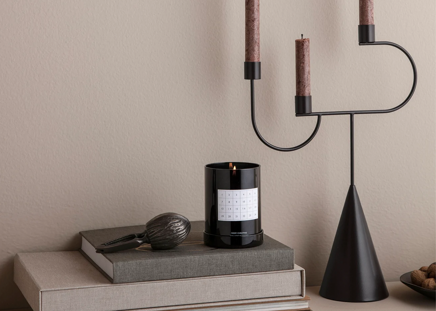 Avant Candelabra Black by Ferm living on a table next to a candle and book.