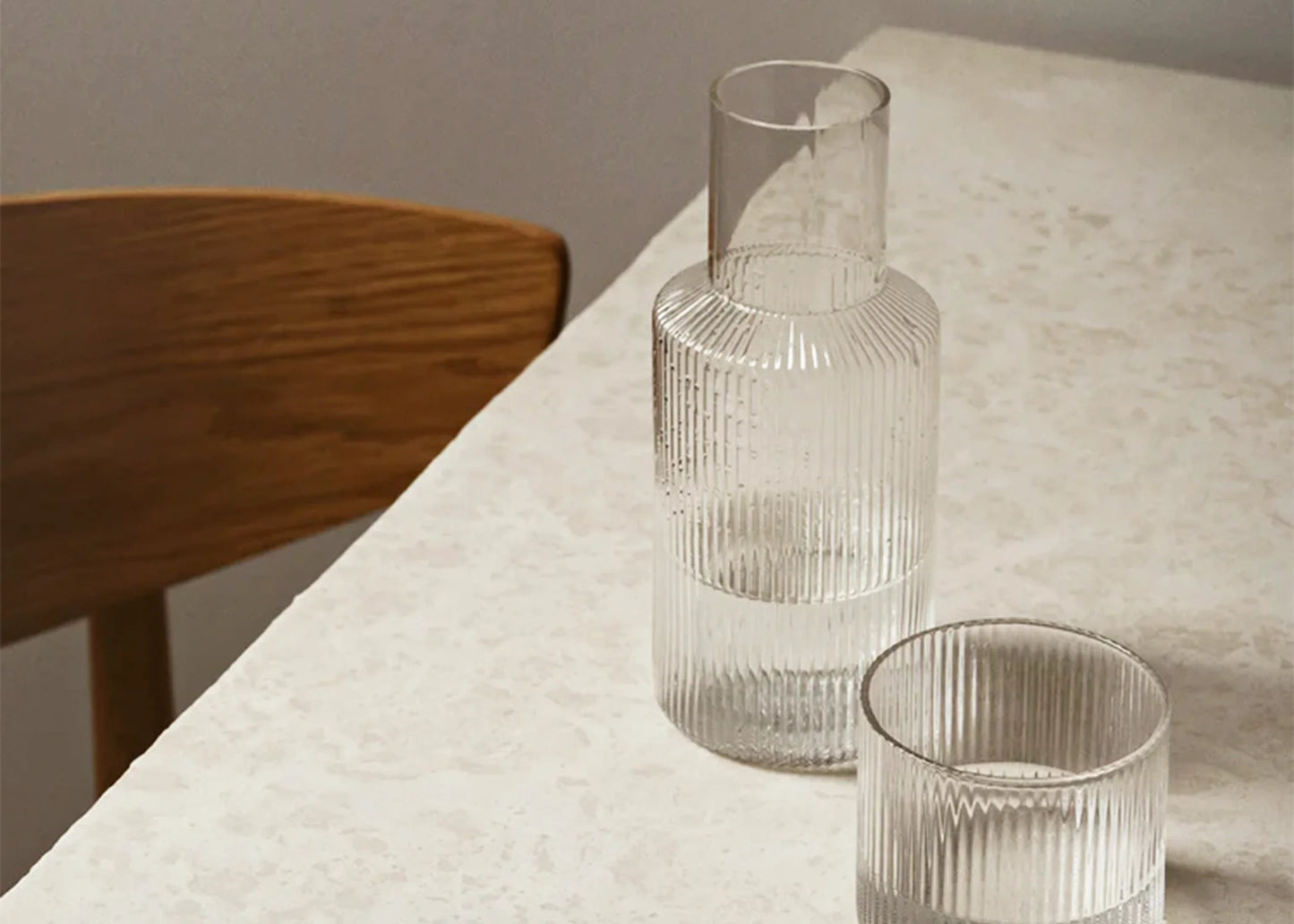 
                  
                    The small glass clear ripple carafe by Ferm Living on a dining room table with water in it.
                  
                