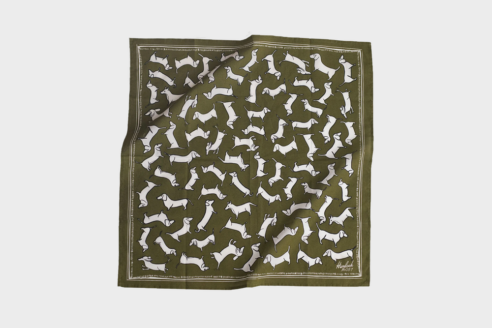 A green bandana with white illustrations of dogs on it by Hemlock Goods No.057 Trixie Bandana as sold by Woodland Mod.
