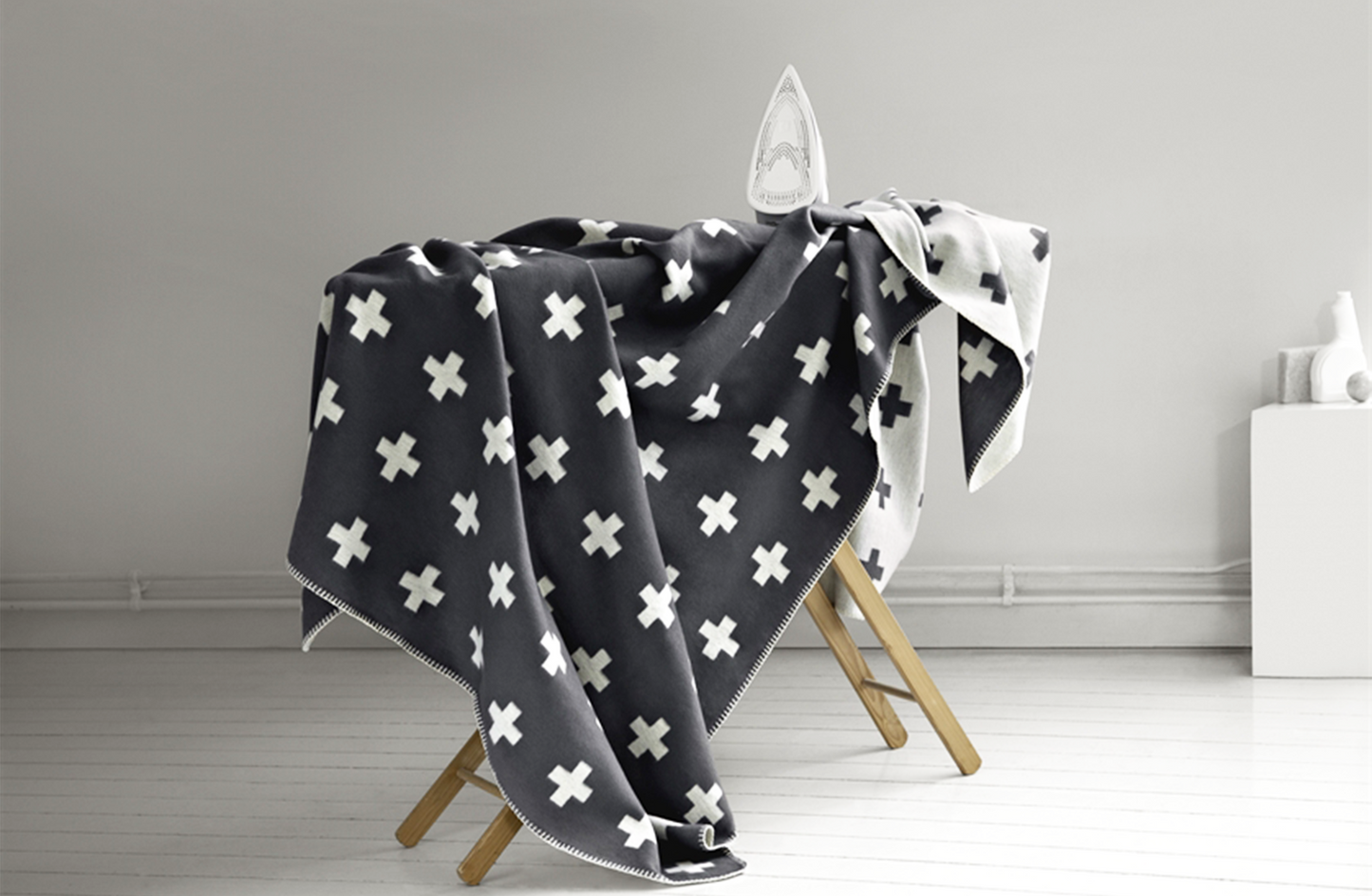 
                  
                    A grey blanket with white crosses on it draped over an ironing board
                  
                