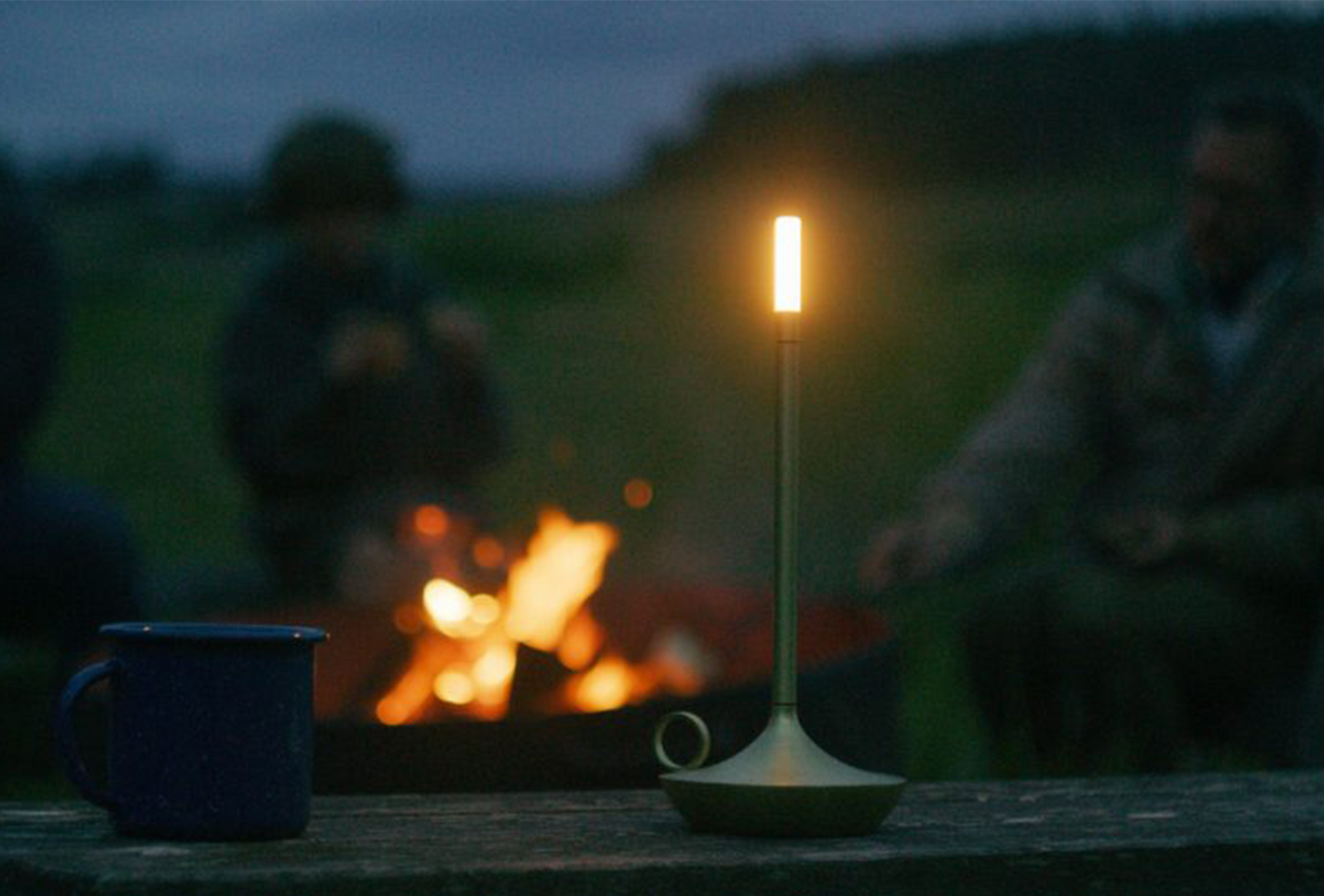 A illuminated Graphite Wick Lamp in front of a blazing fire outside on an evening night