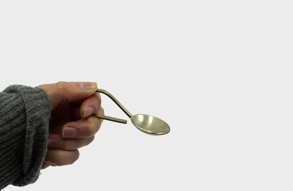 The Fein Sprinkle Spoon in brass by Ferm Living being held by a hand