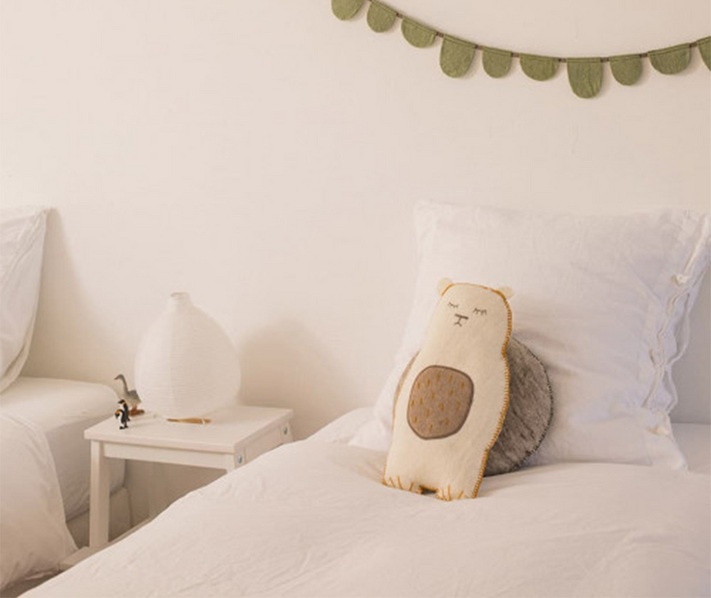 
                  
                    A white teddy bear with gold stitches rested against pillows on a bed.
                  
                